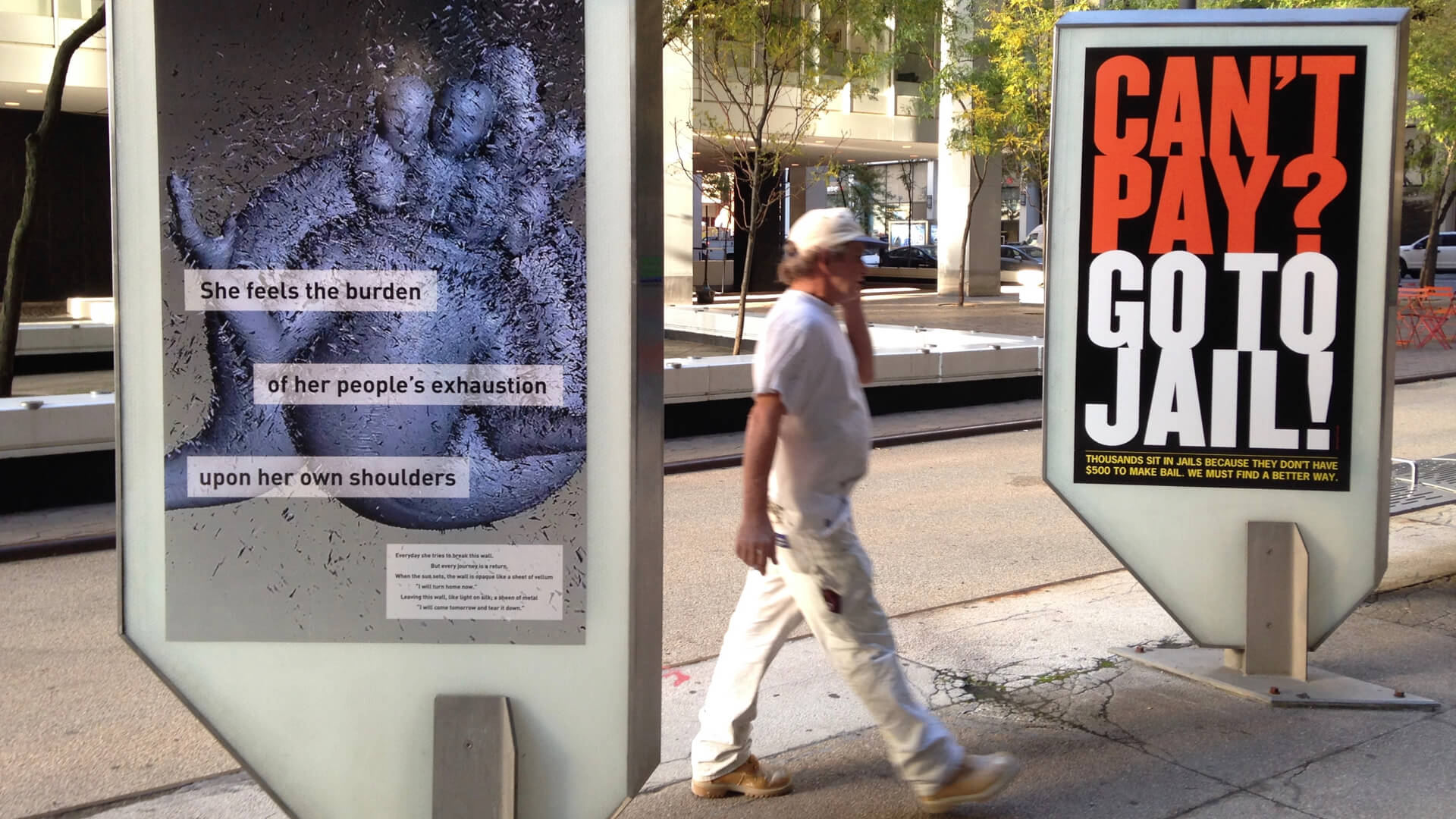a person in overalls walks past two posters