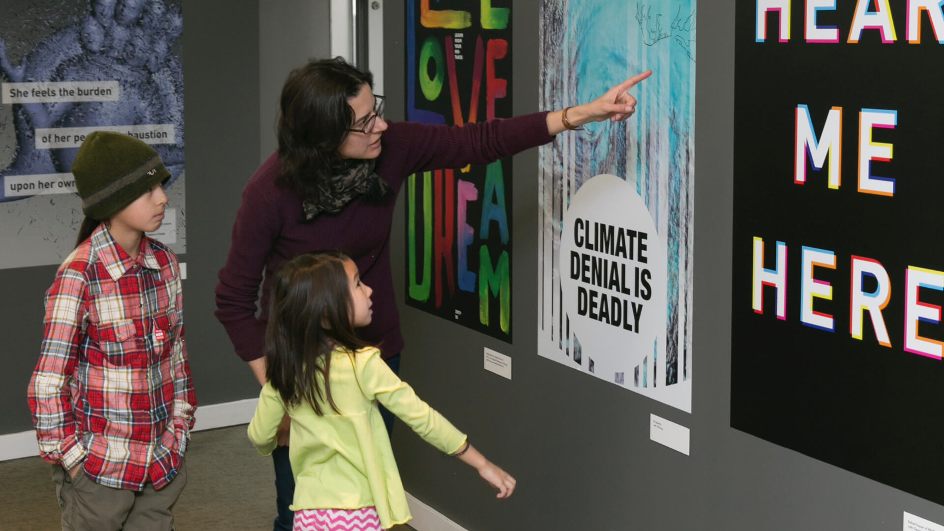 adult points to a poster with two children beside them